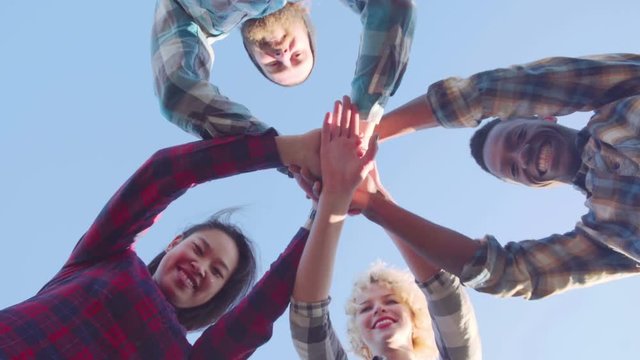 4K From below view of four friends putting their hands one on another, smiling and embracing .