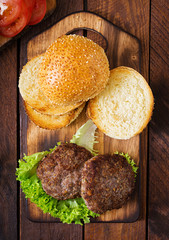 Ingredients for a sandwich - hamburger burger with beef, pickles, tomato and red onion on wooden background. Top view
