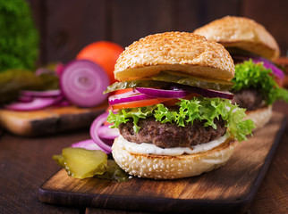Big sandwich - hamburger burger with beef, pickles, tomato and tartar sauce on wooden background.