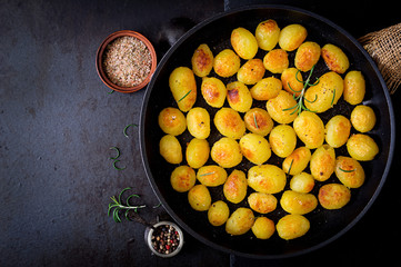 Obraz na płótnie Canvas Baked potatoes with rosemary and pepper in a frying pan on black background. Top view