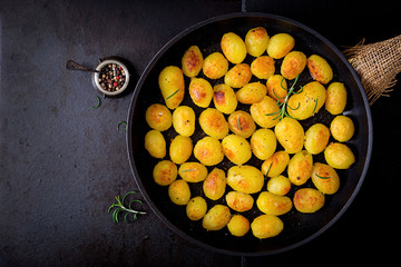Baked potatoes with rosemary and pepper in a frying pan on black background. Top view