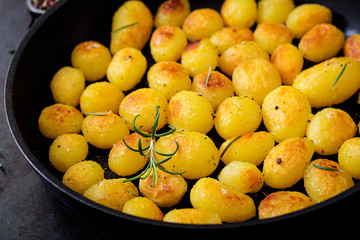 Baked potatoes with rosemary and pepper in a frying pan on black background