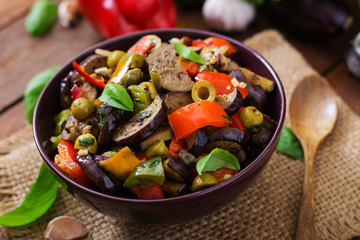 Hot spicy stew eggplant, sweet pepper, olives and capers with basil leaves.