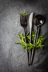 Set of cutlery and rosemary on black stone slate background.