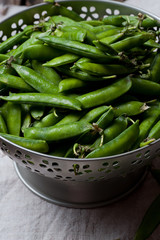 Green peas in steel bowl on wooden background with a linen napkin. Rustic style.