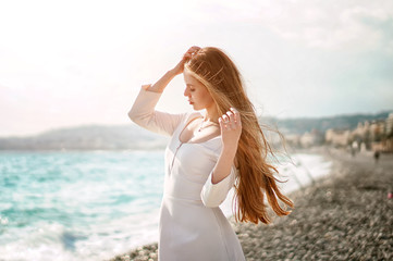 Fototapeta na wymiar Outdoor summer portrait of young pretty woman with great hair looking to the ocean at europe beach, enjoy her freedom and fresh air, wearing stylish white dress.