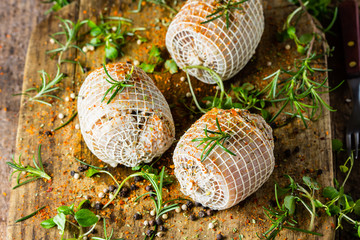 Pork rolls with spices and seasoning on old cutting board