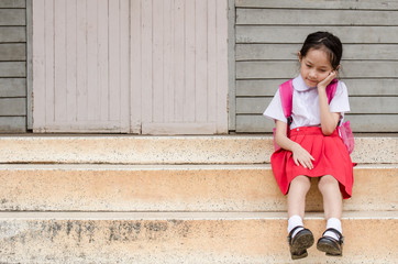 Asian little schoolgirl in uniform sitting at school waiting for