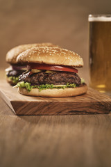two homemade burgers on olive board on oak table with beer