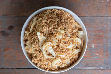 Stir fried instant noodle with mixed vegetable and fried egg in white bowl over the wood table
