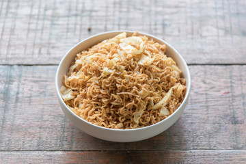 Stir fried instant noodle with mixed vegetable and fried egg in white bowl over the wood table