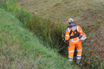 Arbeiter in orange Overall trimmt den Rasen mit einem Trimmer