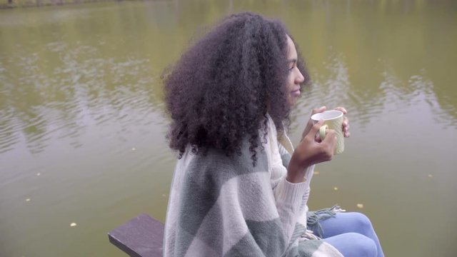 Cute black girl wrapping herself in woolen plaid and drinking hot tea