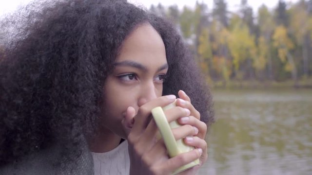 Cute black girl wrapping herself in woolen plaid and drinking hot tea