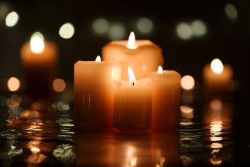 Four burning candles with reflection and candlelight background