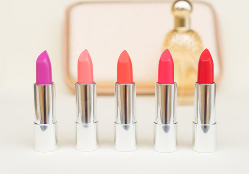 Collection Of Puple, Pink And Red Shiny Lipsticks In Front Of Gold Woman Pursue