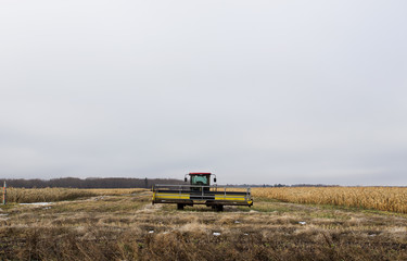 Fototapeta premium A swather parked in a swathed row in corn crop under overcast sky in late autumn