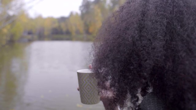 Cute black girl wrapping herself in woolen plaid and drinking hot tea
