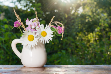 Букет садовых цветов в кувшине на столе в саду в лучах солнца