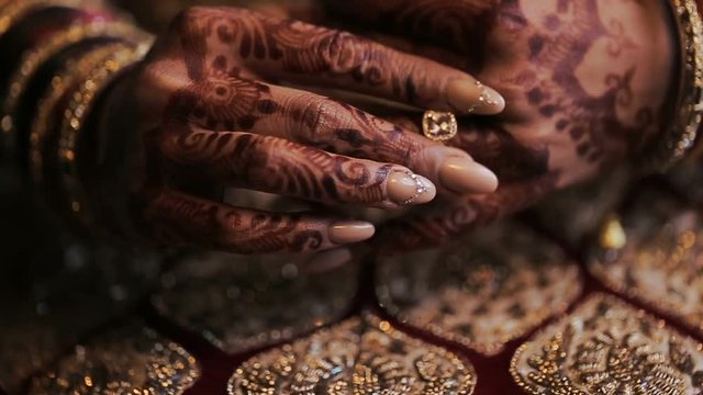Bride's arms pained with mehndi lie on her red dress with golden design
