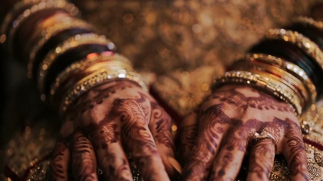 Bride's arms pained with mehndi lie on her red dress with golden design