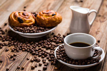 Coffee cup with milk jug and cinnabons on wooden background.