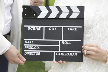 Obraz premium Happy beautiful bride and groom, woman holds clapper board, cinema board