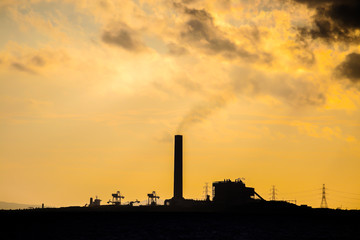 Power plant factory silhouette over sunset at sea