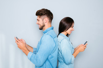 Two lovers standing back to back and chatting on smartphones