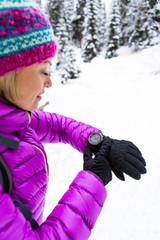 Woman hiker checking sports watch in winter woods and mountains