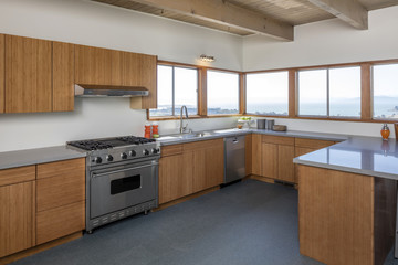 Wooden kitchen in modern home with sea view and stainless steel appliances. 