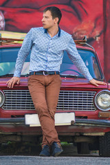Confident wealthy young man near old red car