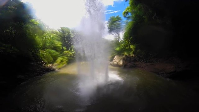 A view of a tropical waterfall from behind as it pours into a natural freshwater pool.