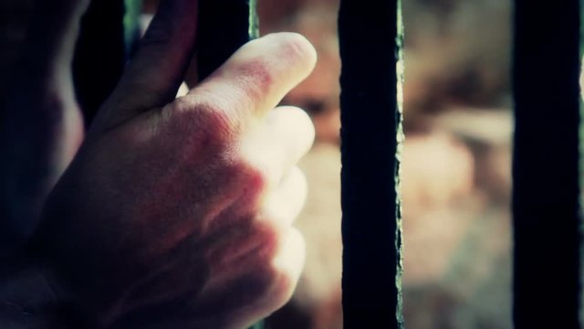 Man in prison grabbing on to bars, upset. Color Corrected for effect.
