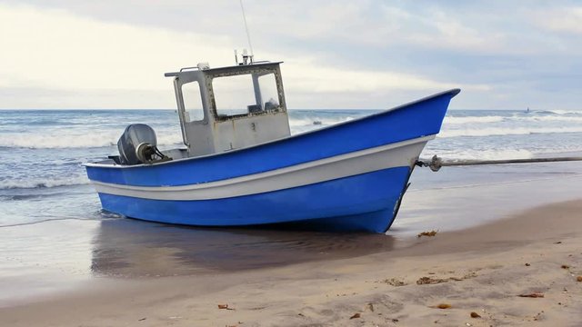 A blue fishing boat rests on the shore of a beach between trips.