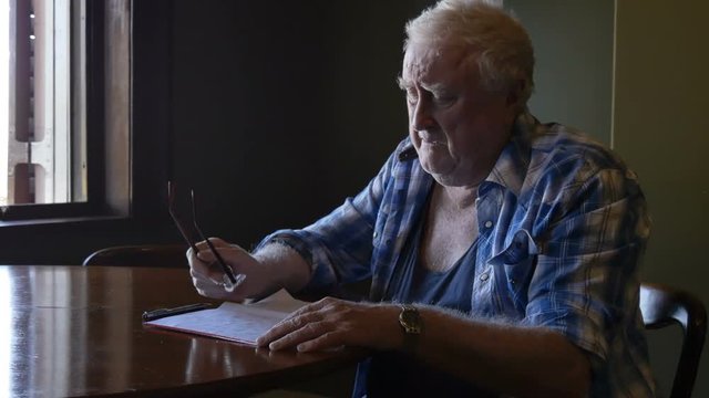 Sad old elderly man in retirment pondering letter at table