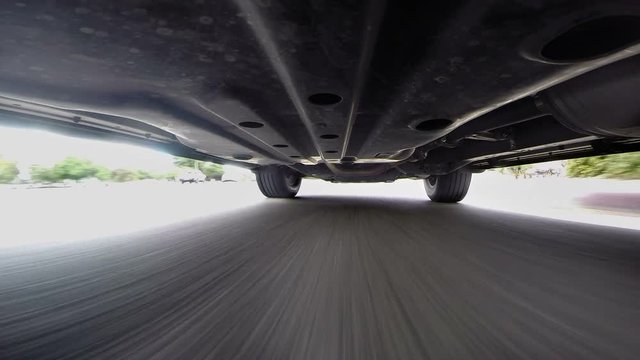 A camera is mounted on the underside of a car to provide POV perspective while driving on an asphalt road. .
