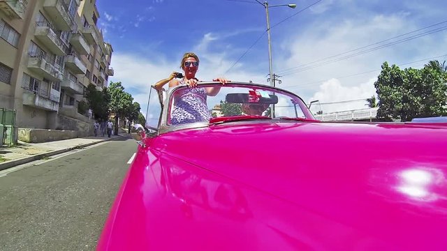Happy people driving through the Havana city in the pink cabriolet car.Camera fixed at the car, moving camera.Many holes on the roads cause shaking of footage.