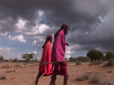 Masai warriors walking along savannah.Dramatic sky in the background