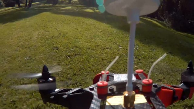 Racing drone quad copter flying FPV through trees in park on sunny day