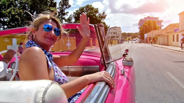 Happy, caucasian woman greeting from a cabriolet.Drive through Havana city, Cuba.Slow motion, high speed camera.Flare light