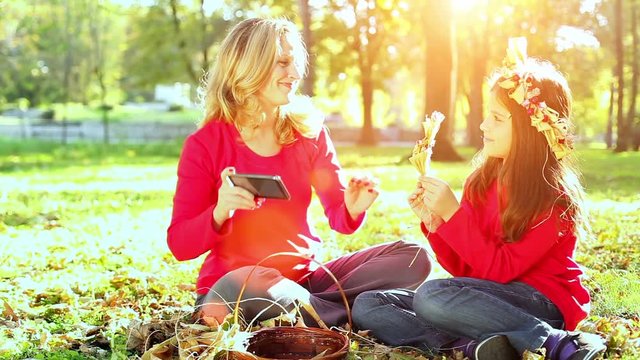 Mother and daughters having fun in autumn park, photographing them selves with tablet and smiling. Sunset light