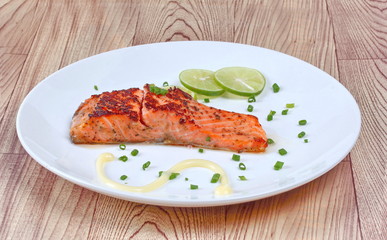 Grilled salmon topped minced shallot ,mayonnaise and sliced lemon on white dish. Isolated.