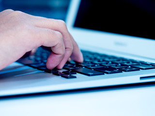Woman hand typing on laptop keyboard. Hand with laptop typing in blue color tone. Selective focus.