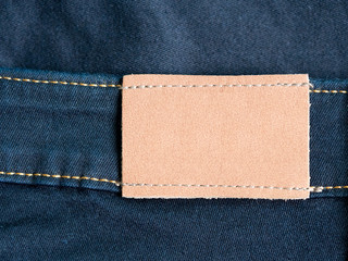 Empty brown leather tag with jean and seam in background. Highly detailed closeup of blank leather label tag on blue jeans.