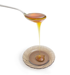 Spoon with honey above glass saucer on a light background