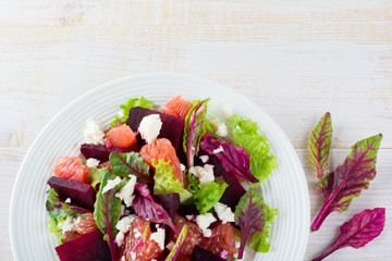 Salad of beets, lettuce, beetroot leaves, grapefruit and feta cheese on a light background. Top view. Place for text. Selective focus.