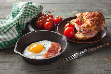 fried eggs with bacon and croissant with sausage on an old wooden background, selective focus