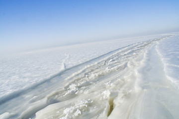 Obraz premium Snowy road track on the frozen ice water. North pole is infinite. Antarctic winter, a dangerous road to the North. The vast icy expanse to the horizon.