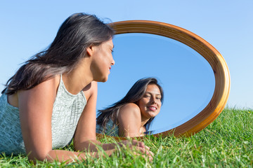 Woman lying on grass outside looking in mirror